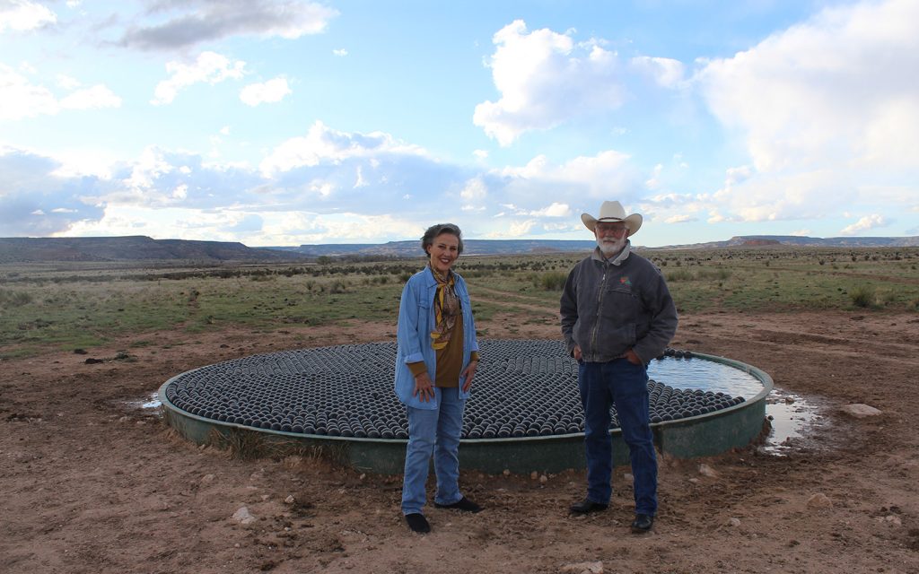 Tuda and Jack Crews stand in front of a stock tank nearly covered in floating shade balls.