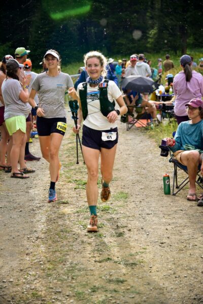 A smiling female runner crosses the finish line of the Crazy Mountain 100.